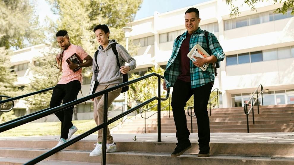 Three students descend an outdoor staircase on a college campus, carrying backpacks and course materials. Photo: RDNE Stock project / Pexels