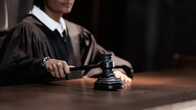 A judge in a black robe holds a gavel over a wooden desk, preparing to make a ruling in the courtroom.