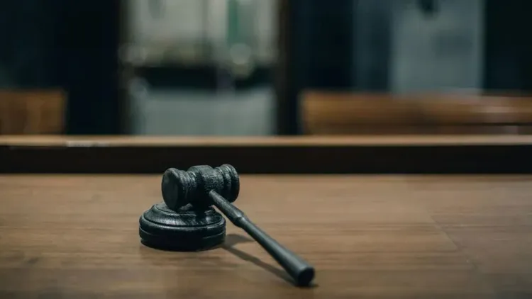 A black wooden gavel rests on its block atop a judge’s bench in an empty courtroom.