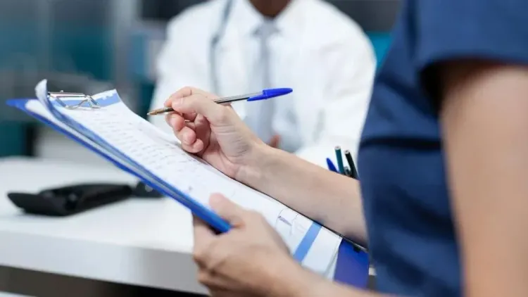 A patient fills out a medical form on a clipboard while seated in a hospital office.