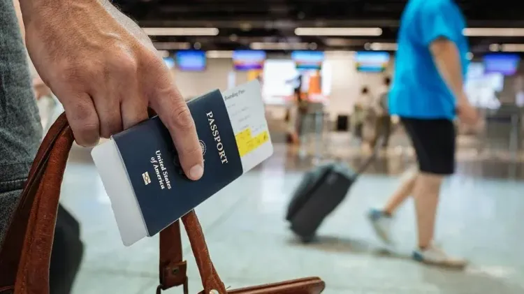 A traveler holds a U.S. passport and boarding pass as they walk through an airport terminal.