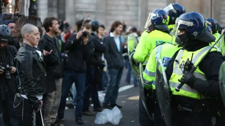 A protester stands in front of a line of police officers in riot gear during a public demonstration.