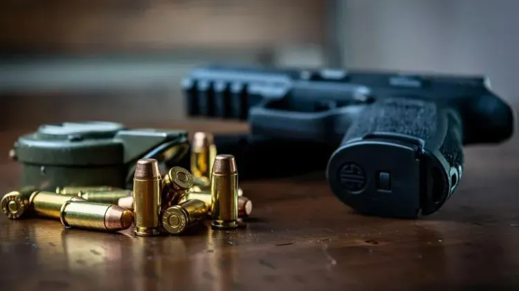 A handgun and ammunition sit on a wooden table.