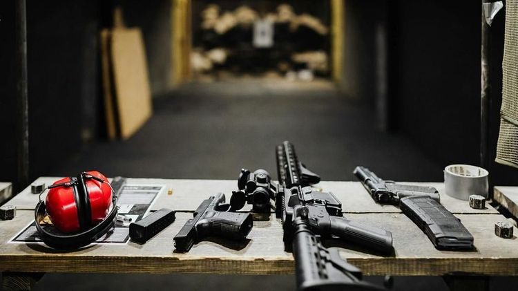 A handgun, rifle, magazines, and protective earmuffs are laid out on a table at an indoor shooting range. Photo: Kaboompics.com / Pexels