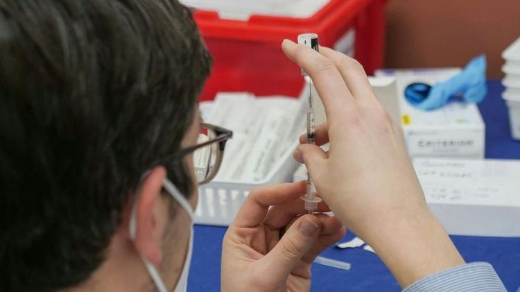 A healthcare worker prepares a syringe with a vaccine dose at a medical station.