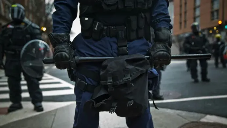 A riot police officer holds a baton while standing in formation during a city deployment.