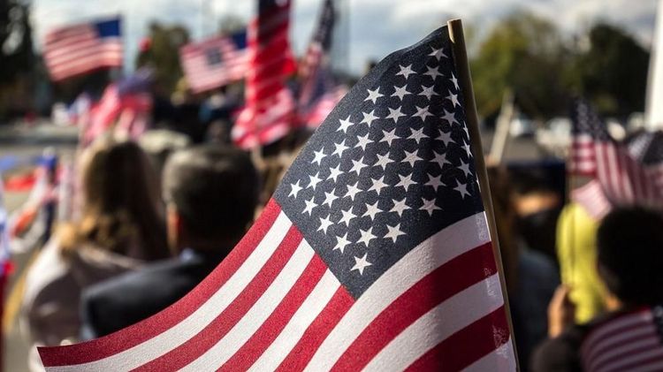 An American flag is held at a rally as more flags wave in the background. Photo: ninjason1 / Freepik