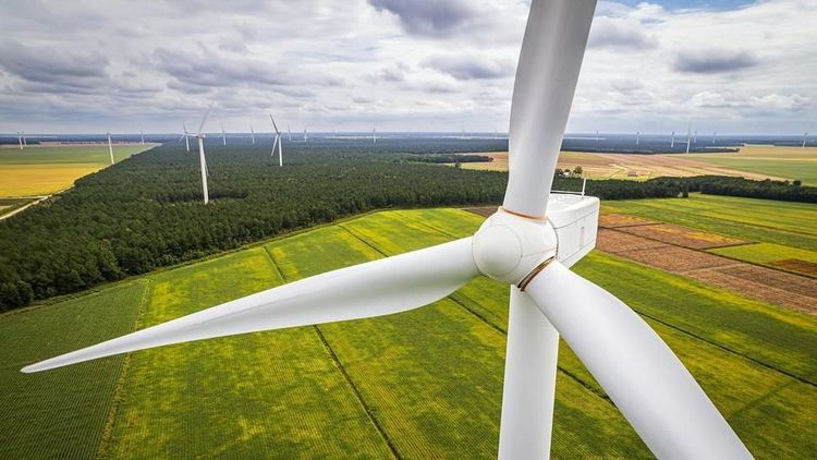 A close-up view of a wind turbine’s blades with farmland and forest stretching into the distance. Photo: Mark Stebnicki / Pexels