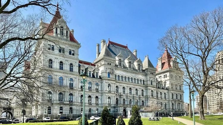 The New York State Capitol stands on a clear spring day with trees and pedestrians in the foreground in Albany, N.Y. 