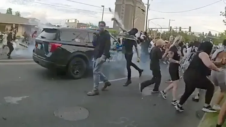A protester throws a smoke canister back toward Spokane police officers and sheriff’s deputies during a demonstration.