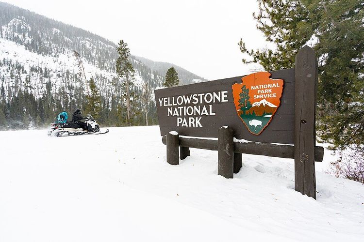 A Snowmobiler rides past the Yellowstone National Park East Entrance sign.