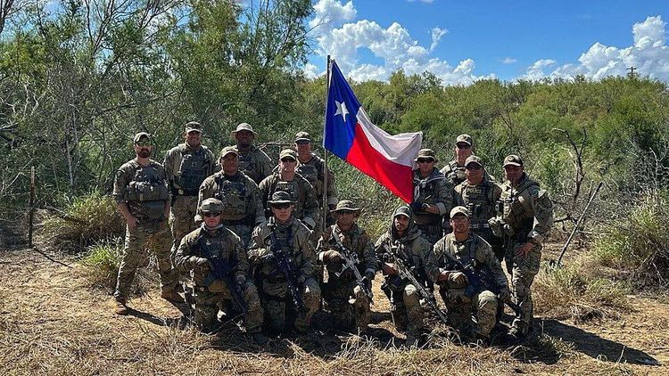 Texas National Guard and state law-enforcement personnel pose with the Texas flag in brush near Eagle Pass, Maverick County, Feb. 22, 2024, during Operation Lone Star deployments along the Rio Grande.