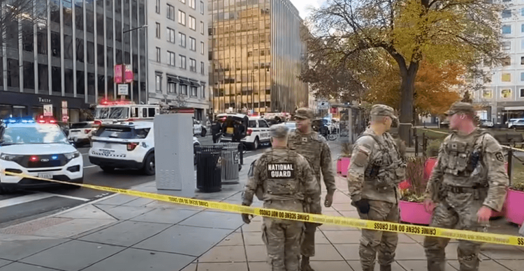 Guardsmen behind crime scene tape with police cars in the background.