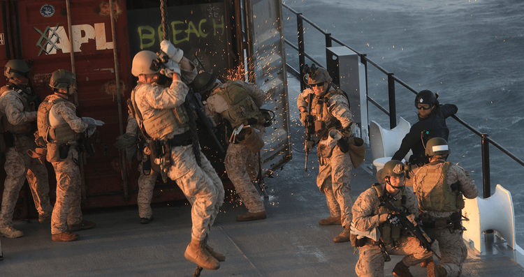Marines with the 1st Marine Special Operations Battalion breach a cargo container as others rappel from a CH-47 helicopter during Visit, Board, Search and Seizure (VBSS) training