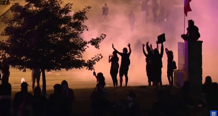Protestors are gathered in front of a background of teargas and smoke during the assault on the White House in late May, 2020